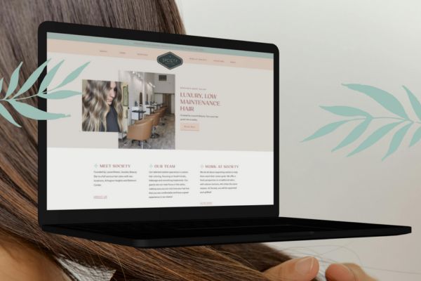 WordPress Websites 11 A modern laptop displaying a luxury hair salon website with a sleek design, featuring images of styled hair, salon interiors, and informational sections. The background includes soft leaf illustrations and a close-up of a woman's hair.